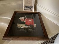 Both framed Coca-Cola advertisements side by side
