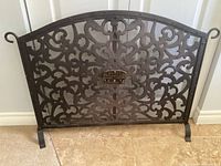Full view of arched wrought iron fireplace screen showing scrollwork and feet