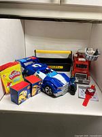 Group shot showing all toys including race car, fire engine, toolbox, Play-Doh bag, Minions boxes, small vehicle and watch