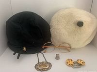 Group view of both hats, eyeglass frames, earrings, thimble, and vodka label