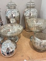 Group shot showing both lidded urns, a ribbed footed bowl, decorative sphere and small hammered bowl