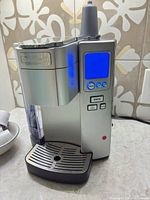 Front view showing coffee maker, display lit, reservoir and drip tray