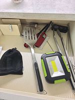 Drawer view showing spatula, LED light, tongs, skewers, mesh bag