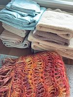 Stacked light blue polka-dot vinyl fabric, beige woven bath mats, beige terry towels, orange knit throw