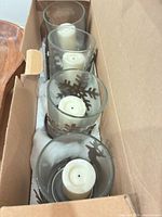 Four glass candle holders with snowflake sleeves and pillar candles in original box