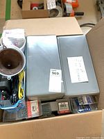 Overview of box contents showing two grey metal tins, brown funnel component, blue bundle, and multiple screw packs