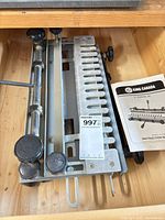 Dovetail jig with clamping bars and fence visible, lot tag attached