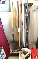 Long-handle shovel, rake, broom heads visible