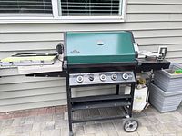 Front view of closed green-hood Napoleon grill on wheeled cart, side burner cover visible, propane tank below