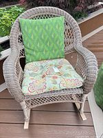 Front view of wicker rocking chair with floral cushion and excluded green pillow
