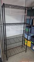 Full view of black metal shelving unit with four shelves and two white hanging baskets