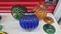 Three colored glass lamp shades and two lids on table