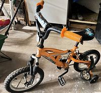 Side view of Supercycle Hi 5 orange kids bike showing frame, wheels, brakes and training wheels