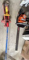 Floor jack and hedge trimmer side by side on concrete