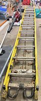 Full length view of yellow fiberglass extension ladder showing aluminum rungs and overall wear