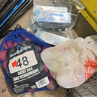 Blue mesh bag labeled value bag containing orange golf balls, plastic bag with Dunlop sleeves nearby