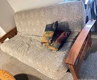 Full view of futon showing beige floral upholstery, wooden frame and two throw pillows