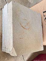 Side view of a gray concrete paver showing thickness and chipped corner