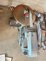 Entire scroll saw laying on floor with cord wrapped, showing table and motor housing