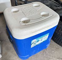 Front and top view of blue Igloo Ice Cube cooler showing wheels, handle stowed, cup holders in lid