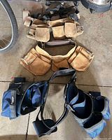Three tool belts laid out: two tan suede, one blue nylon with harness
