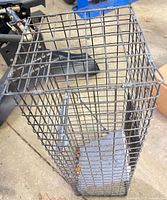 angled top view of tall rectangular steel wire mesh trap showing bait plate at base