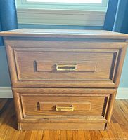 Front view of oak-finish nightstand with two drawers and brass pulls
