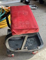 Three-quarter view of red-cushioned creeper stool showing frame, tray, casters