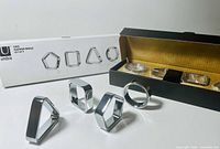Four geometric napkin rings displayed with one open box and one closed box