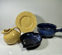 Group shot of all four ceramic items: yellow creamer, yellow plate, blue handled bowl, blue heart-shaped bowl