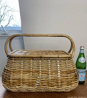 Closed wicker picnic basket next to bottle for scale