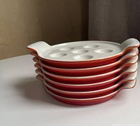 Stacked side view of all six orange escargot dishes showing exterior colour and handle shape