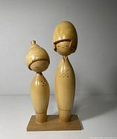 Full view of two unpainted wooden Kokeshi dolls on base
