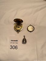 Overview of all three items: pocket compass, Bulova pendant watch and lantern-shaped pendant
