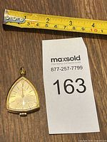 Pendant watch beside measuring tape and lot card showing scale