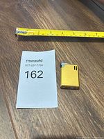 Lighter next to tape for scale, gold rectangular form