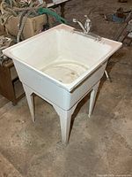 Front angled view of plastic laundry tub showing faucet, legs, internal basin