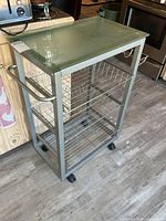 Full view of metal serving cart showing glass top, frame, casters