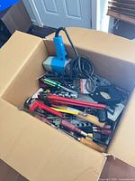 Box containing assorted hand tools and blue corded planer