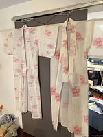 Front view of full-length white kimono with pink floral design hung for display