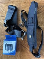 Two camera straps and Partner quick-release mount box displayed on wood surface