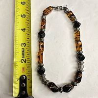 Full necklace next to tape measure showing 18 in length, amber and black glass beads, silver spacers, barrel clasp