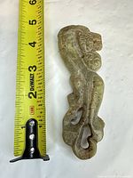 Full view of carved jade belt hook beside tape measure showing approximately 5 inch length