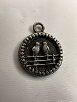 Front of round bird pendant showing two birds on fence and oxidized finish