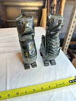 Front view of both stone figurines beside measuring tape