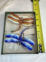 Both enamel dragonfly ornaments in box with measuring tape showing length