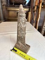 Front view of pink and gray speckled granite falcon-headed figurine with tape for scale