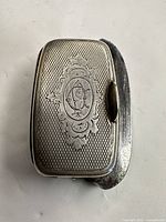 Front view showing engraved decoration and monogram on vesta case