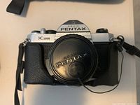 Front view of Pentax K1000 body with lens cap and strap attached
