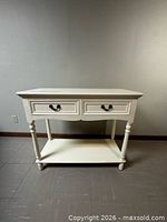 Front view of off-white console table showing two drawers, turned legs, lower shelf